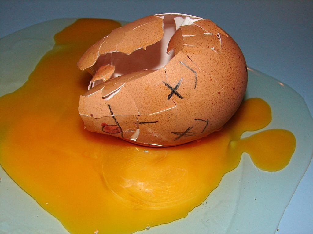 pic of broken egg. face of dead person drawn on broken shell, laying in the yolk and egg white that has spilled out